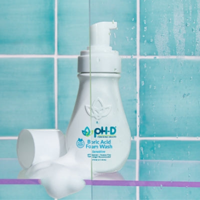 pH-D Feminine Health Boric Acid Foam Wash bottle on a shower shelf with foam, set against a teal tiled background, showcasing gentle cleansing for sensitive skin.