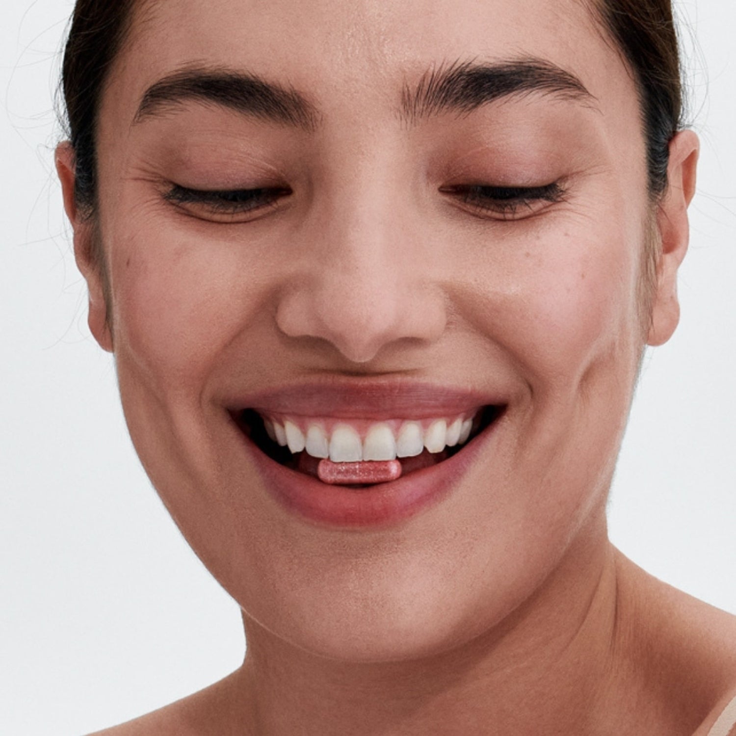 Smiling woman holding a PhD Feminine Health probiotic supplement between her teeth, emphasizing wellness and gut health.